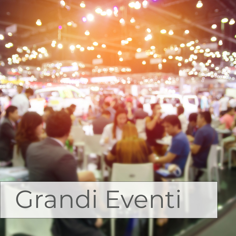 molti tavoli con persone sedute e, sullo sfondo, una esposizione di automobili